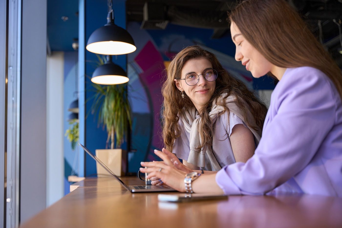 Two colleagues in a one-to-one conversation across a timber desk.