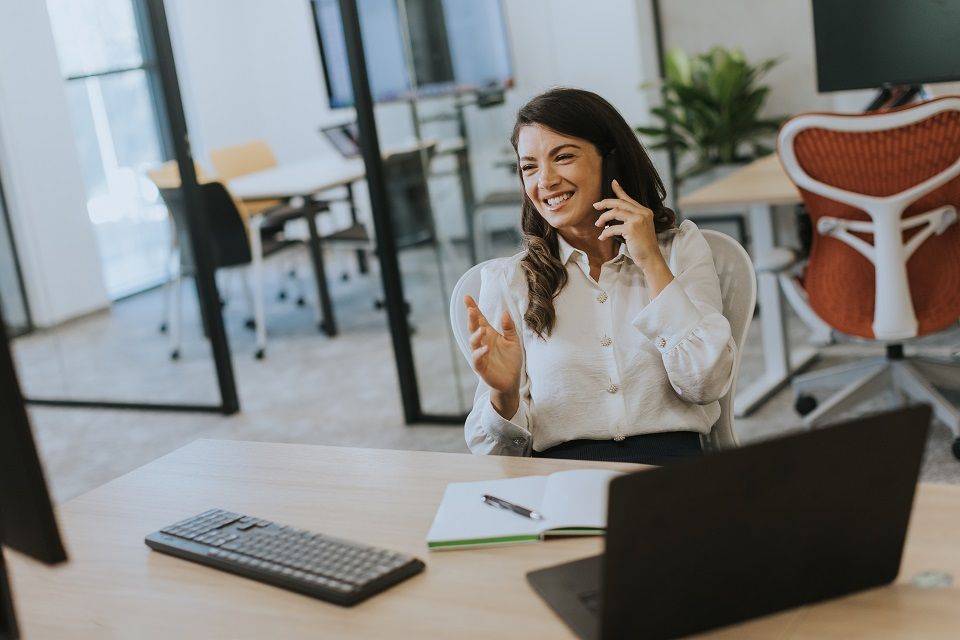 A leader gesturing while talking on the phone at a desk in a daylit office.