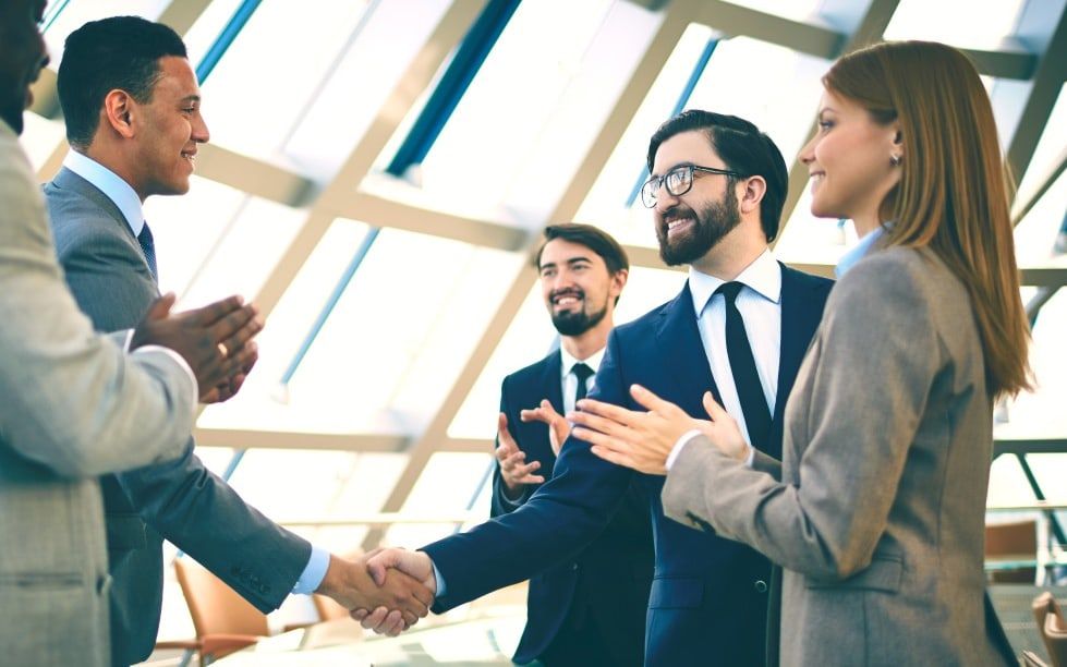 A group of business colleagues greeting one another in a glass-walled atrium.