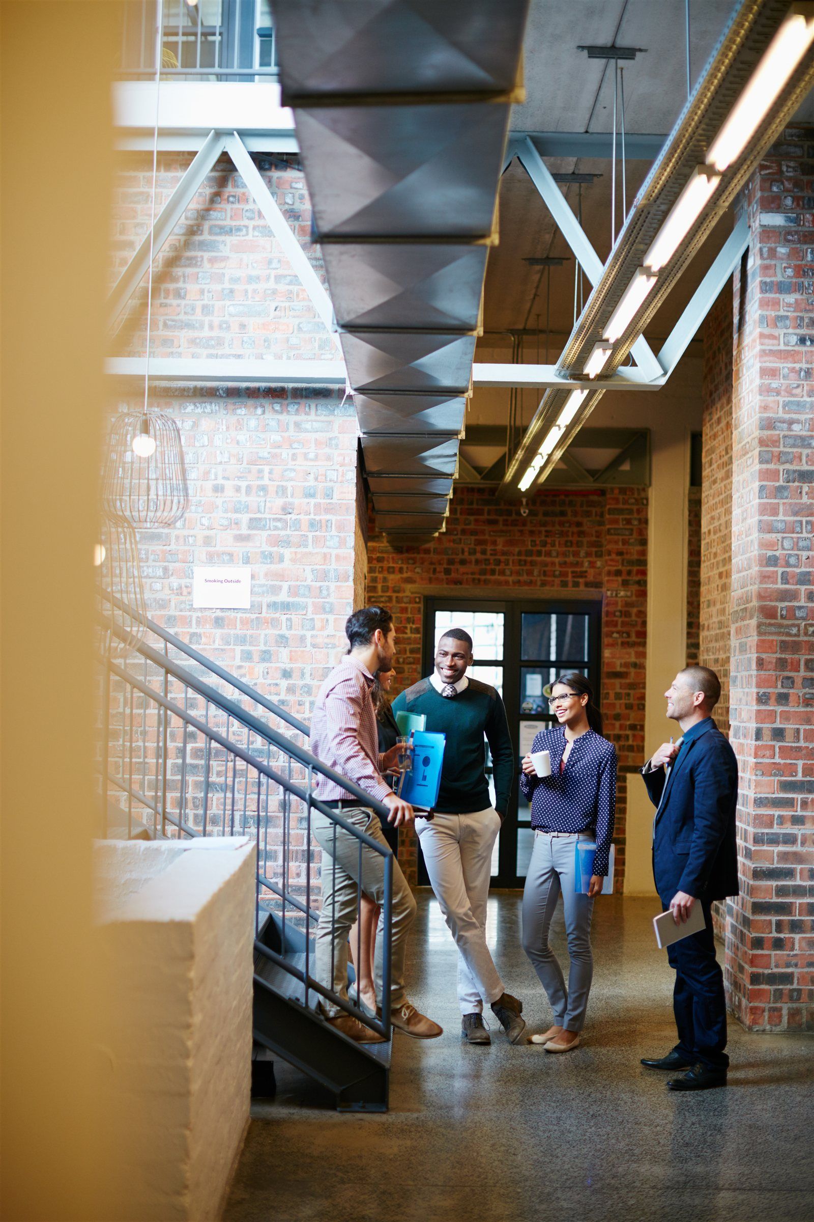 Colleagues talking on a brick-walled staircase landing in a loft office.