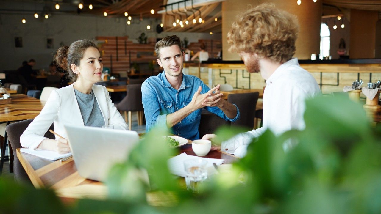 Three colleagues in conversation across a timber table in a daylit café.
